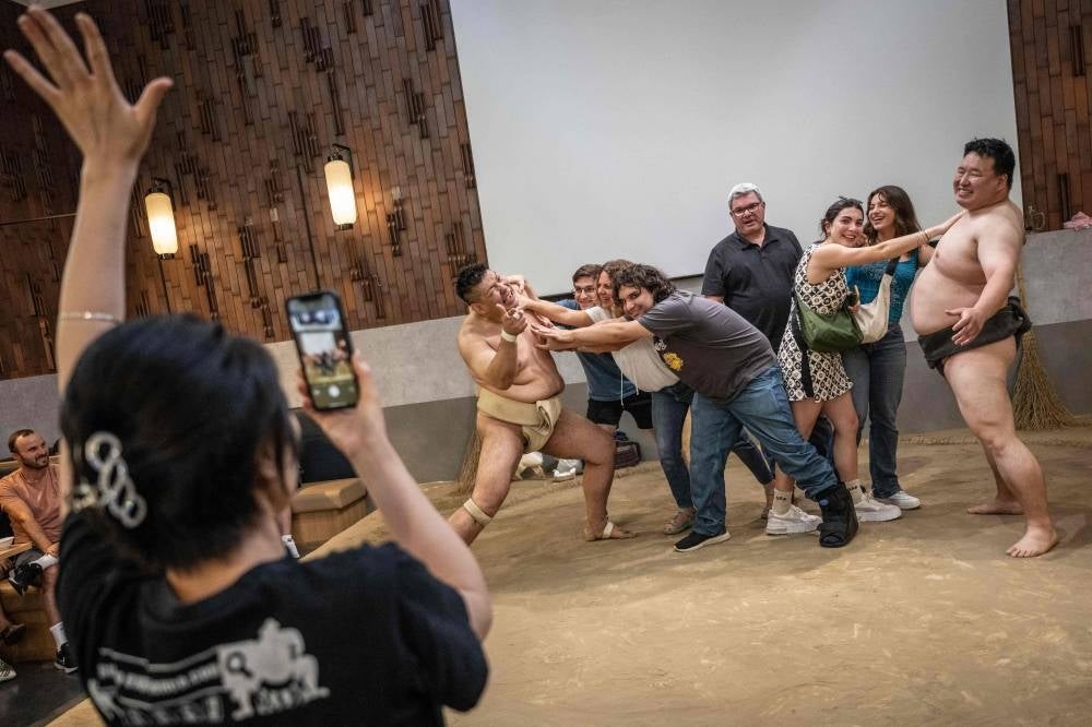 Foreign tourists posing for photographs with former sumo wrestlers at the Yokozuna Tonkatsu Dosukoi Tanaka restaurant in Tokyo. (Photo by Yuichi YAMAZAKI / AFP)