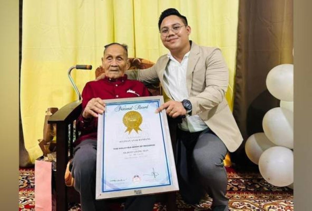 Seliman Bandang and his grandson Michael with a Malaysia Book of Records certificate denoting him as the country’s oldest man - AWANI Michael Bandang 