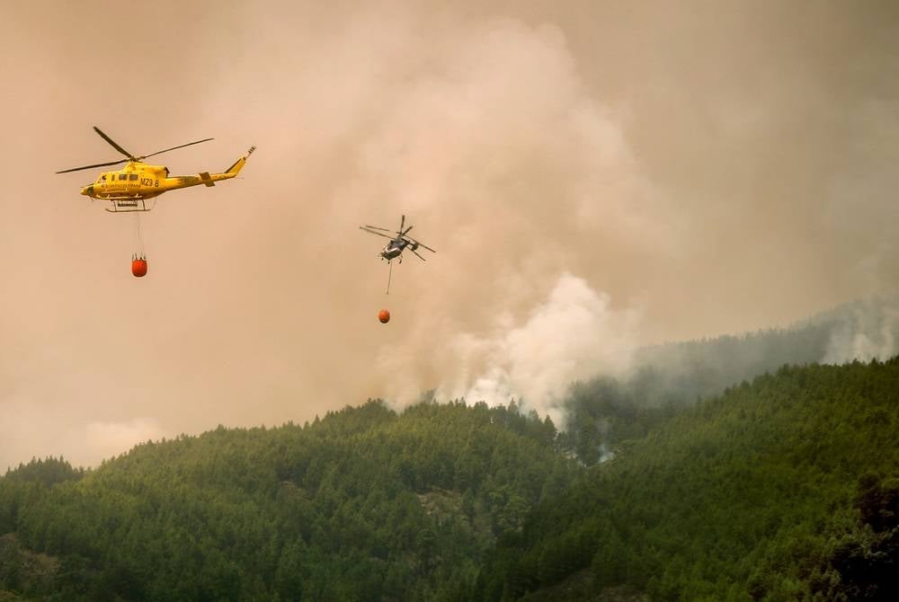 Helicopters fly over the area of Pico Cho Marcial in Arafo to drop water over a huge wildfire raging through forested areas that surround the Mount Teide volcano natural park, on the Canary island of Tenerife, on Aug 20, 2023. (Photo by DESIREE MARTIN / AFP)