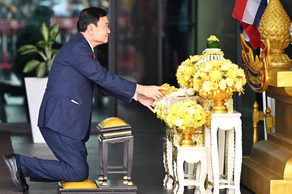 Former Thai Prime Minister Thaksin Shinawatra prepares to bow in homage to the king's portrait after landing at Bangkok's Don Mueang airport. Photo by Manan Vatsyayana/AFP