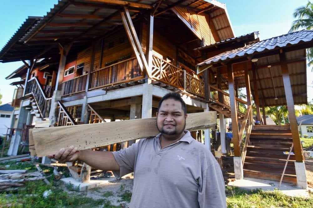 Nazmie, standing in front of the house he built from discarded wood at Pantai Senok. Photo by Bernama