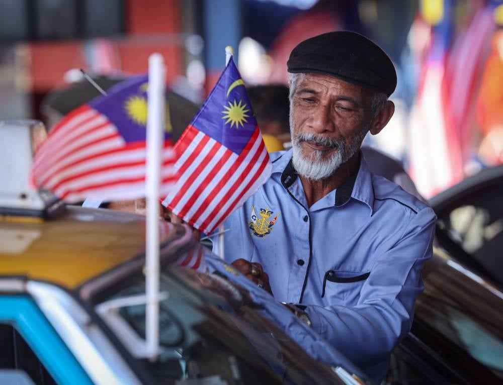 The driver of the Tuan Tuan Punya Car Rental Association of Muar Hassmoro Dohar, 69, installing the Jalur Gemilang on his vehicle at the Bentayan Taxi Stand, today to celebrate the 66th National Day Celebration. (PHOTO BERNAMA) 