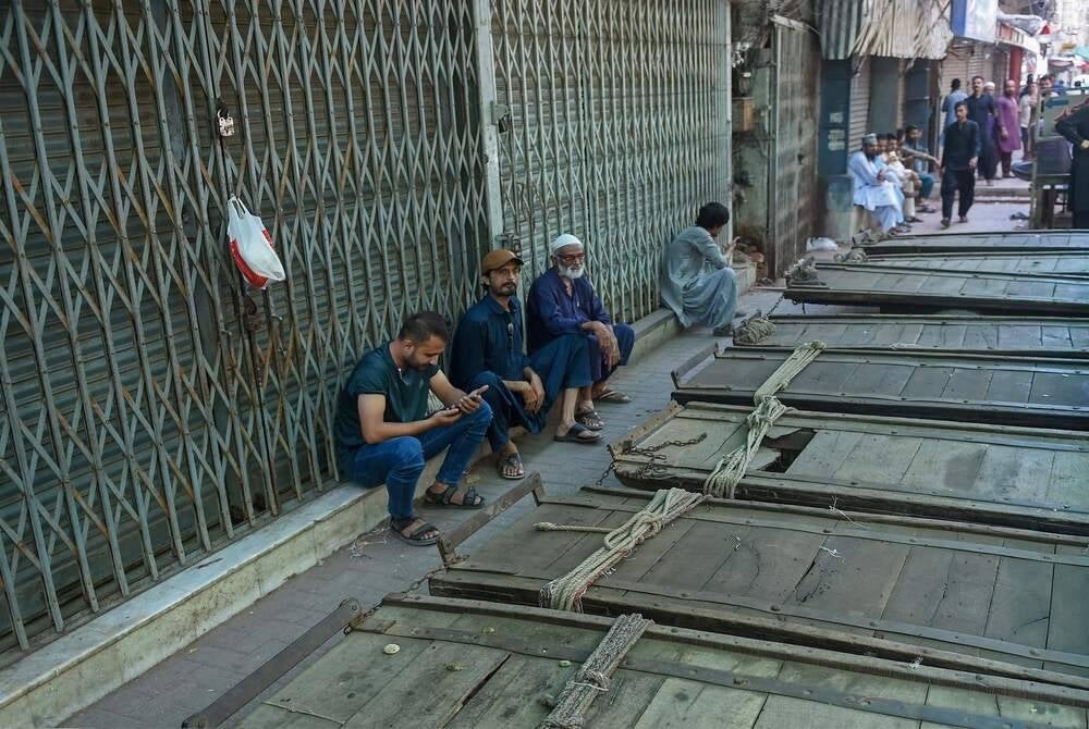 Shopkeepers sit beside carts outside closed shops along a roadside in Karachi on Sept 2, during a nationwide strike against the surge in electricity and fuel prices. (Photo by Rizwan TABASSUM / AFP)