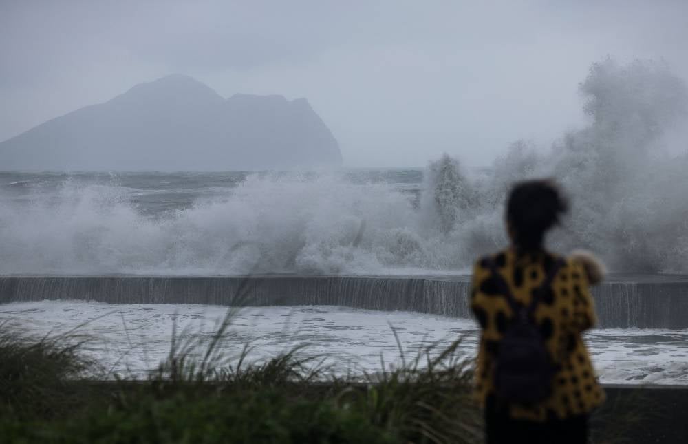 A woman holds her dog while watching the waves in Yilan as Typhoon Haikui makes landfall in eastern Taiwan on Sept 3, 2023. - Photo by I-Hwa Cheng / AFP