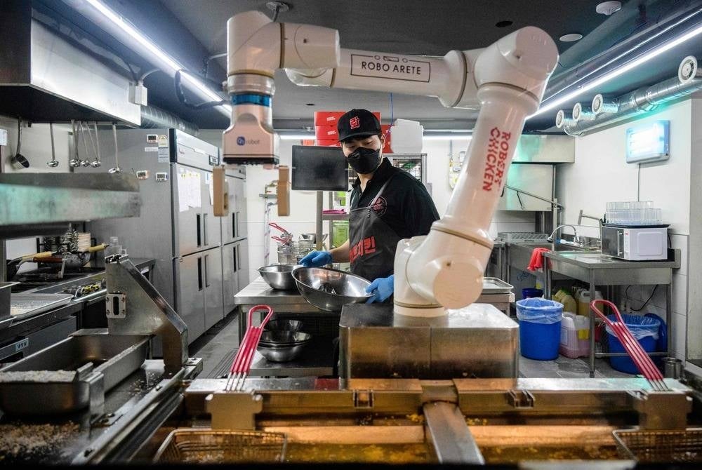 In this photo taken on June 13, an employee walks past a robot being used to fry chicken, at a Robert Chicken restaurant in Seoul. (Photo by Anthony WALLACE / AFP)
