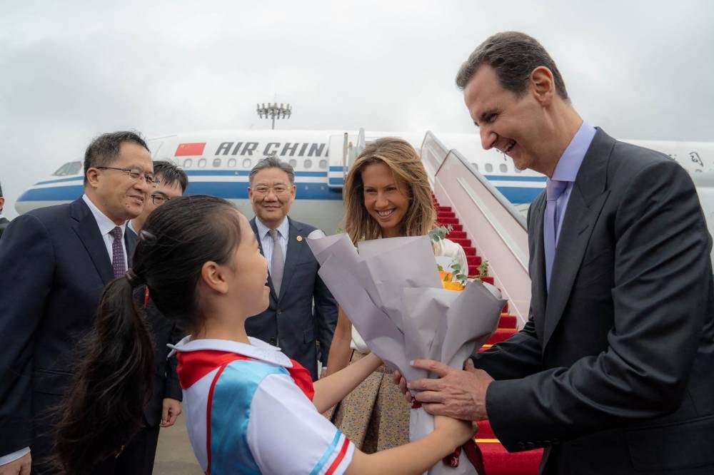 A handout picture released by the official Syrian Arab News Agency (SANA) shows Syria's President Bashar al-Assad (R) and First Lady Asma al-Assad (2-R) being welcomed upon their arrival at the airport in Beijing - AFP 