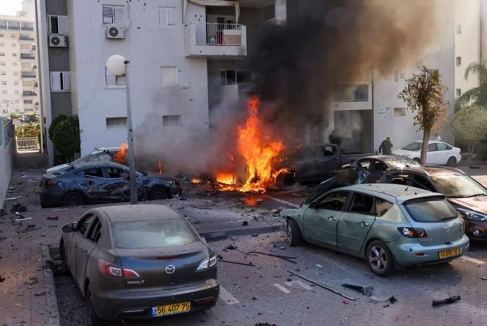 TOPSHOT - A member of the Israeli security forces stands near burning cars following a rocket attack from the Gaza Strip in Ashkelon, southern Israel, on Oct 7. (Photo by Ahmad GHARABLI / AFP)