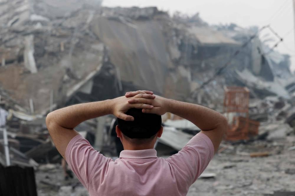 A Palestinian man stands early on October 8, 2023 in front of the rubble of Gaza City's Al-Watan Tower, which was destroyed in an Israeli airstrikes. - Photo by AFP