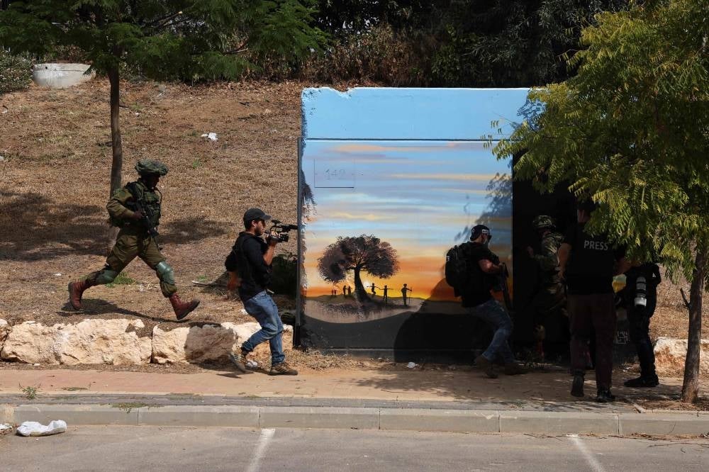 Security forces and journalists take cover during a rocket attack from the Gaza Strip, in the southern city of Sderot on October 8, 2023. - Photo by AFP