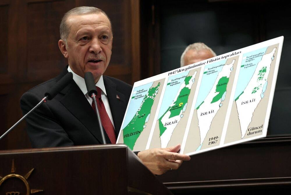 Turkish President and AK Party Chairman Recep Tayyip Erdogan holds a sign showing the evolution of lands of Israel and Palestine on maps at his party's group meeting in the Turkish Grand National Assembly in Ankara on Oct 11. (Photo by Adem ALTAN / AFP)