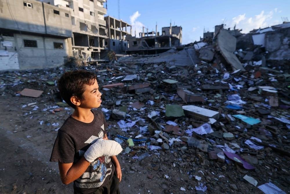A wounded Palestinian boy, 12-year-old Mohammed Sofi, looks at buildings destroyed during Israeli airstrikes near his home in the Rafah refugee camp in the southern of Gaza Strip on Oct 16. (Photo by MOHAMMED ABED / AFP)