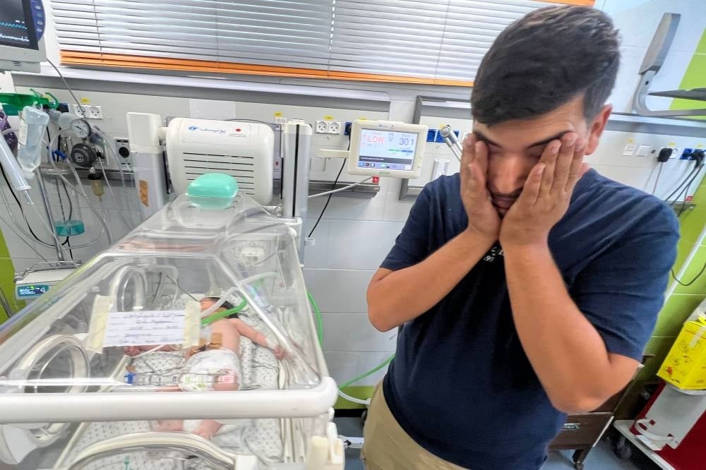 Ayman Abou Chamalah stands next to his daughter Mecca, as she receives care inside an incubator at a hospital in Rafah. Photo by Mai Yaghi/AFP