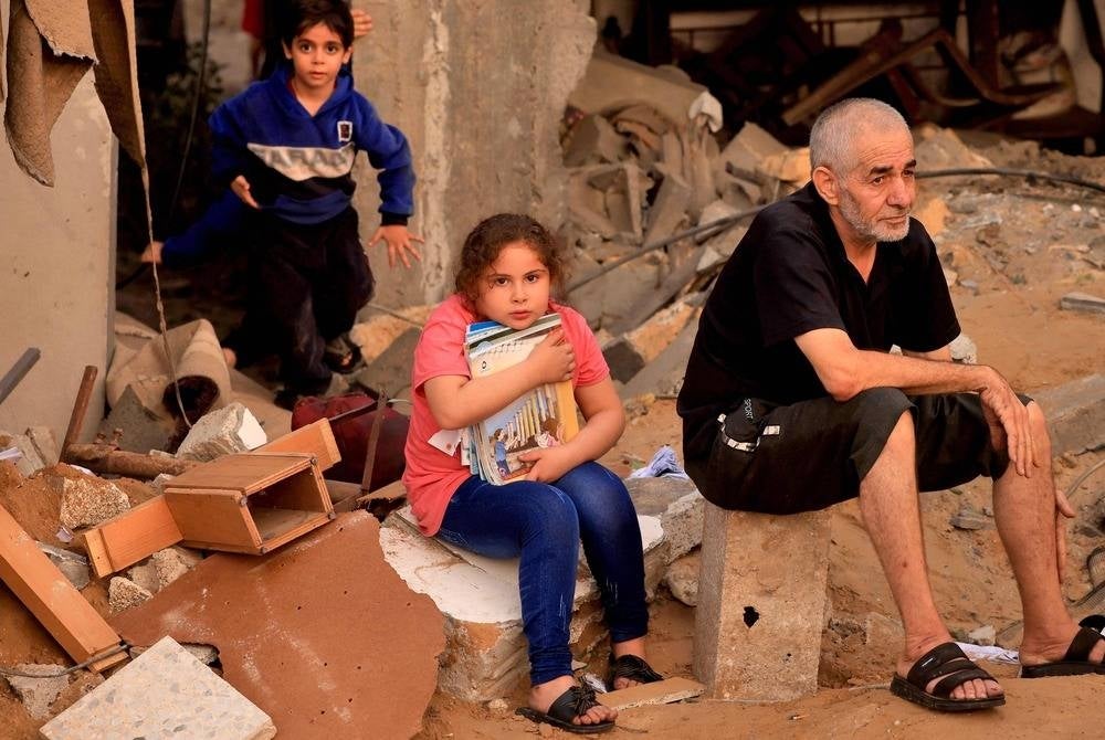 A Palestinian girl clutches salvaged books as people look for survivors in the rubble of a destroyed building hit in an Israeli strike in Khan Yunis in the southern Gaza Strip on Oct 24, amid the ongoing battles between Israel and the Palestinian group Hamas. (Photo by MAHMUD HAMS / AFP)