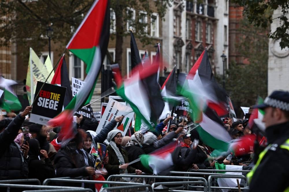 Protesters hold up placards and wave Palestinian flags at the gates of Downing Street after taking part in a 'March For Palestine' in London on Oct 28. Photo by Henry Nicholls/AFP