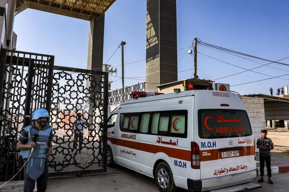 A journalist stands by as Palestinian health ministry ambulances cross the gate to enter the Rafah border crossing in the southern Gaza Strip before crossing into Egypt on November 1, 2023. - Photo by AFP