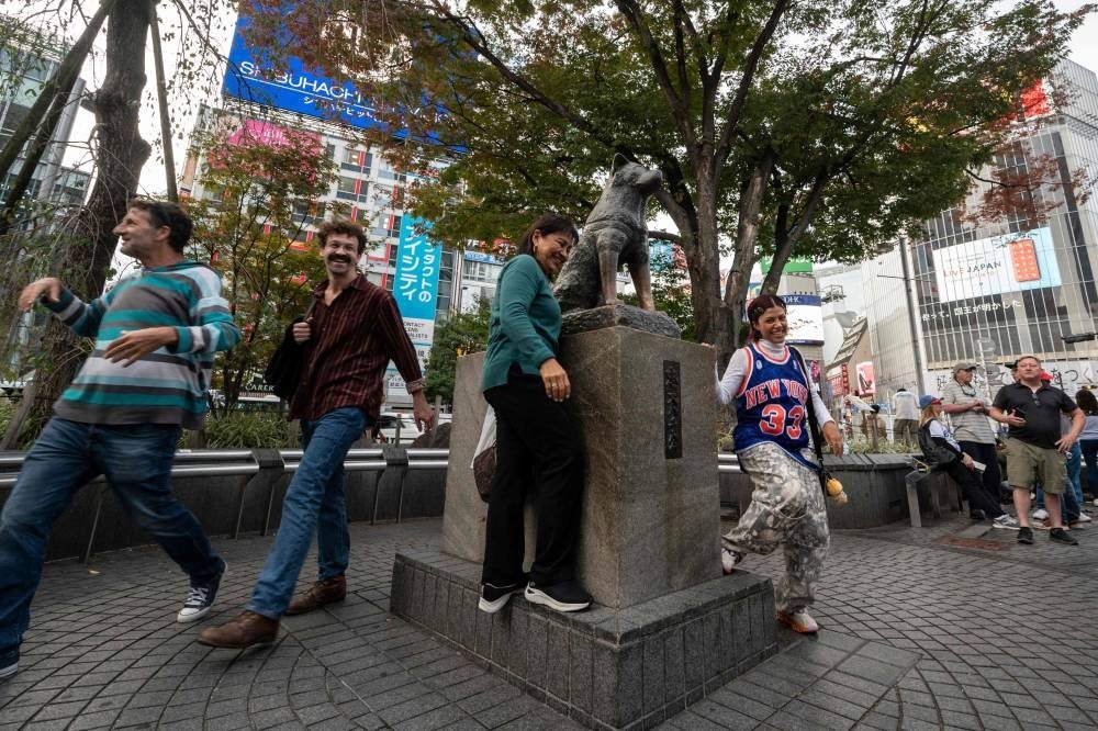 People pose for photos next to the statue of "Hachiko" in front of Shibuya station in central Tokyo on November 6, 2023, ahead of the 100th anniversary of the legendary dog's birth this month. - Photo by AFP