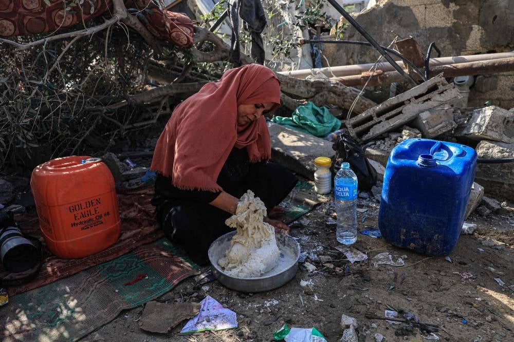 Nesrine, Amal al-Robayaa's sister-in-law, mixes flour with water to make bread amid the ruins of the family home destroyed in an Israeli strike in Rafah in the southern Gaza Strip, on November 7, 2023 - AFP