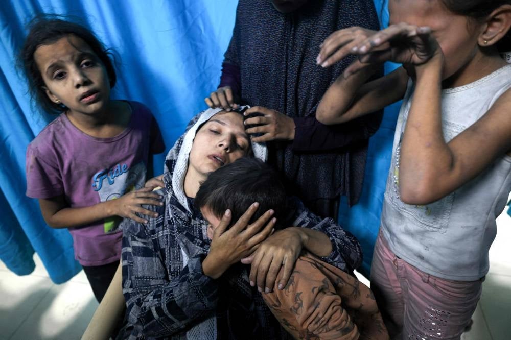 A wounded Palestinian woman from the Baraka family is surrounded by her children upon their arrival at Nasser Hospital in Khan Yunis in the southern Gaza Strip following Israeli air strikes that hit their building on November 13, 2023 - AFP 