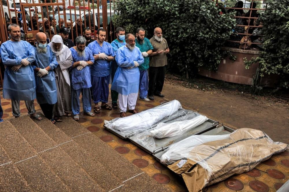 Physicians and other men pray before some of the bodies of victims who were killed in Israeli bombardment before their burial, outside the morgue at Nasser hospital in Khan Yunis in the southern Gaza Strip on November 14, 2023 - AFP 