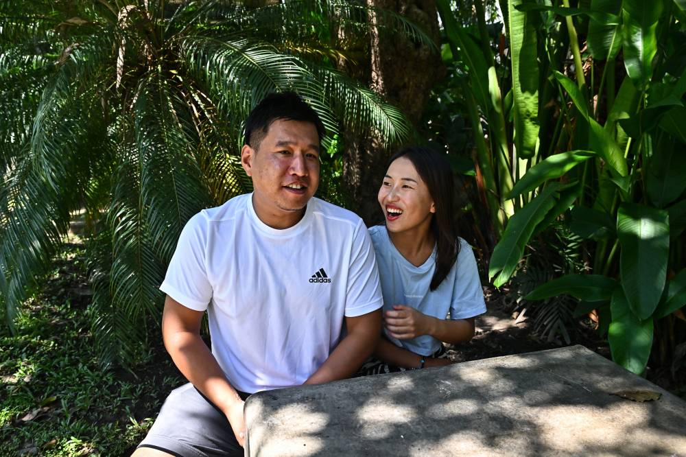 This photo taken on October 20, 2023 shows Chinese nationals Connie Chen, 26, (R) and her husband Gordon Lin, 32, (L) sitting together outside their apartment in the northern Thai city of Chiang Mai. (Photo by Lillian SUWANRUMPHA / AFP)