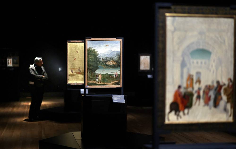 A visitor looks at a painting called "Landscape with a hunter and fishermen" (C) by an anonymous artist, as part of the Reversos exhibition, which presents the hidden back sides of renowned paintings, at the Prado Museum in Madrid on December 5, 2023. - Photo by AFP