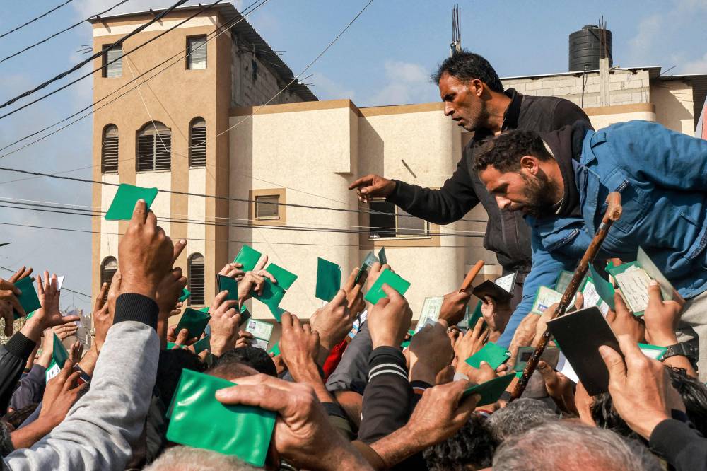 Palestinians wave their identity cards as they gather to receive flour rations for their families outside a warehouse of the United Nations Relief and Works Agency for Palestine Refugees (UNRWA) in Rafah in the southern Gaza Strip - AFP 