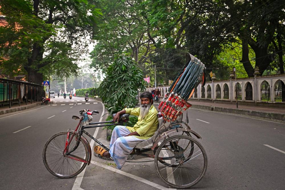 This photograph taken on December 14, 2023 shows bicycle rickshaw driver Mohammad Babu posing for a portrait with his vehicle on a street in Dhaka. - Photo by AFP