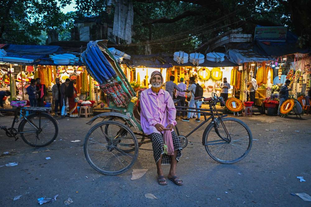 This photograph taken on December 14, 2023 shows bicycle rickshaw driver Rahamat Ullah posing for a portrait with his vehicle on a street in Dhaka. - Photo by AFP