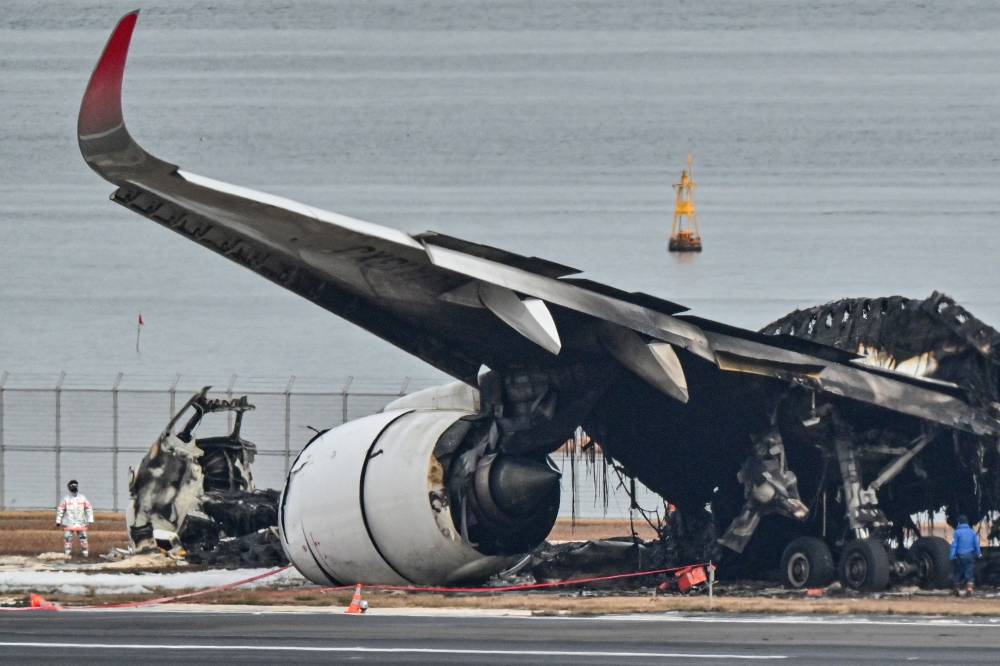 Officials looking at the burnt wreckage of a Japan Airlines passenger plane on the tarmac at Tokyo International Airport at Haneda in Tokyo. - Photo by AFP