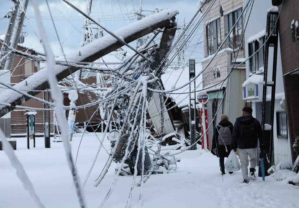 People walk past earthquake damage covered in snow in the city of Suzu, Ishikawa prefecture on Jan 8, 2024, a week after a major 7.5 magnitude earthquake struck the Noto region in Ishikawa prefecture on New Year's Day. - (Photo by JIJI Press / AFP)