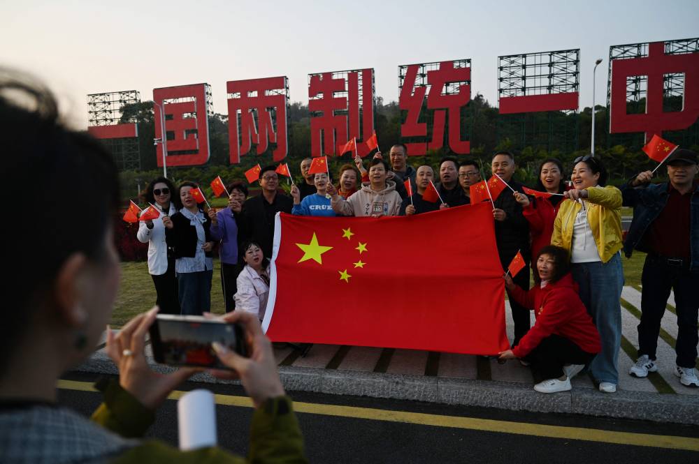 A group poses with a Chinese flag in front of a giant propaganda slogan which reads "One Country, Two Systems, Unify China”, which can be seen from Taiwan’s Kinmen Island, on the beach in Xiamen, in China’s southeast Fujian province on January 10, 2024, days before Taiwan’s Presidential election. (Photo by GREG BAKER / AFP)