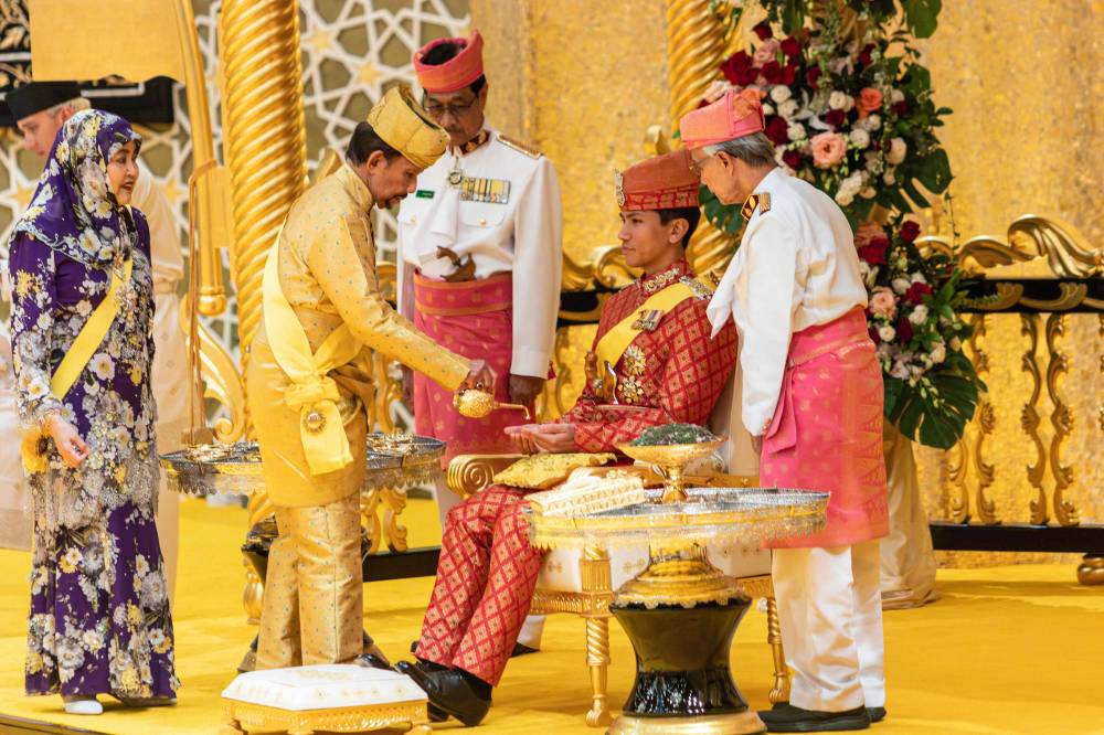 Sultan Hassanal Bolkiah (second from left) pouring scented oil on the hands of Prince Abdul Mateen during the royal powdering ceremony at Istana Nurul Iman, ahead of his wedding to Anisha Rosnah, in Bandar Seri Begawan, as Queen Raja Isteri Pengiran Anak Hajah Saleha (L) looks on. Photo by Rudolf Portillo/AFP