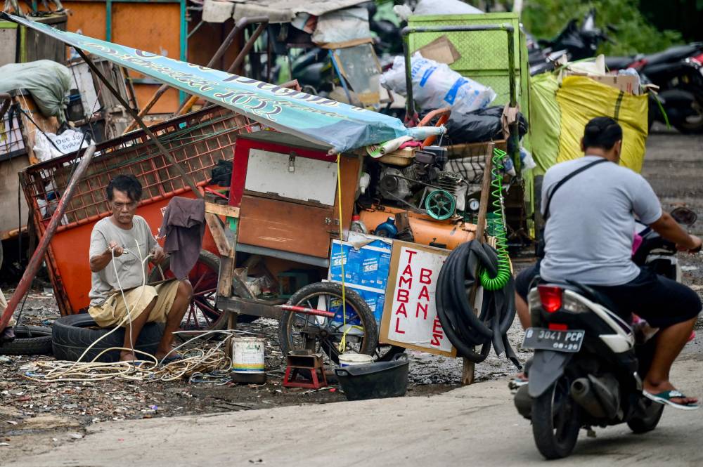 A tire repairman collects copper from a cable for resale while waiting for customers in Jakarta on January 31, 2024. - Photo by AFP