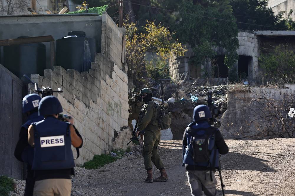 An Israeli soldier takes aim from behind a wall as journalists cover their patrol in the Jenin refugee camp, in the occupied West Bank on Nov 29, 2023, during an ongoing military operation in the camp. - (Photo by ZAIN JAAFAR / AFP)