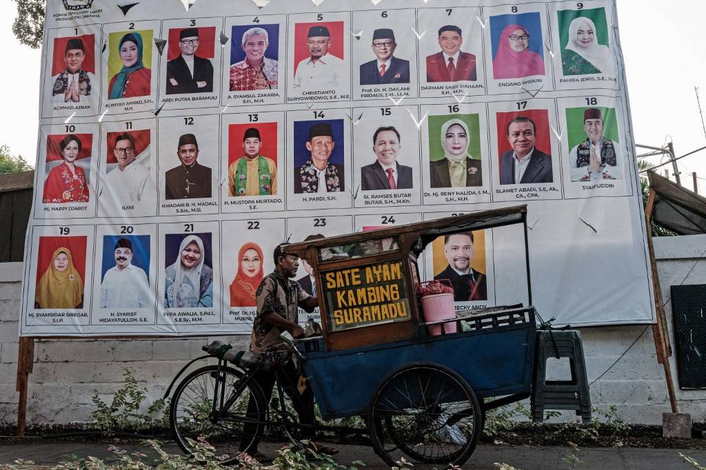 A street food vendor passes by a poster of a list of candidates for members of the Regional Representative Council (DPD) of Jakarta province in Jakarta on Dec 20, 2023, ahead of the voting day of 2024 general election slated for Feb. 14, 2024. - Photo by AFP