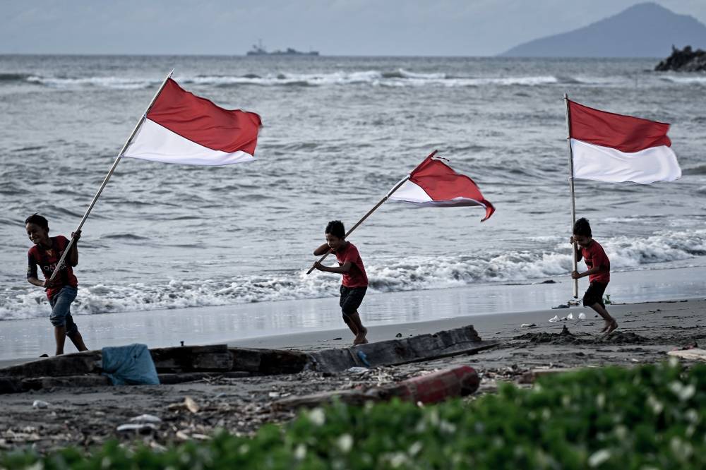 Children run as they hold national flags at a beach in Banda Aceh on Aug 15, 2023, two days before Indonesia's 78th Independence Day. - (Photo by CHAIDEER MAHYUDDIN / AFP)