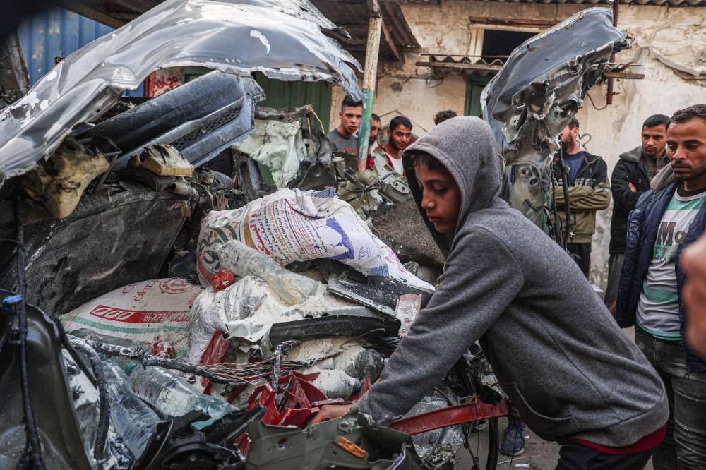A Palestinian youth inspects a car wreck following Israeli bombardment in Rafah in the southern Gaza Strip on Jan 8, 2024. - (Photo by SAID KHATIB / AFP)
