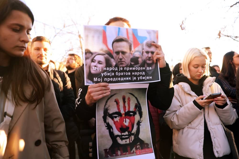 A man holds banners depicting Alexei Navalny with a text reading 'My people is forced to kill brother's people, My President has been murdered' and Russian President Vladimir Putin during a vigil for the late opposition leader and anti-corruption activist Alexei Navalny following the announcement of his death, in front of the Russian Embassy in Belgrade, Serbia, Feb 16. (Photo by EPA/ANDREJ CUKIC)