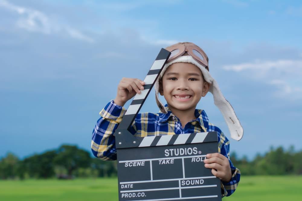 Kid playing film clapper board against summer sky background. Film director concept.