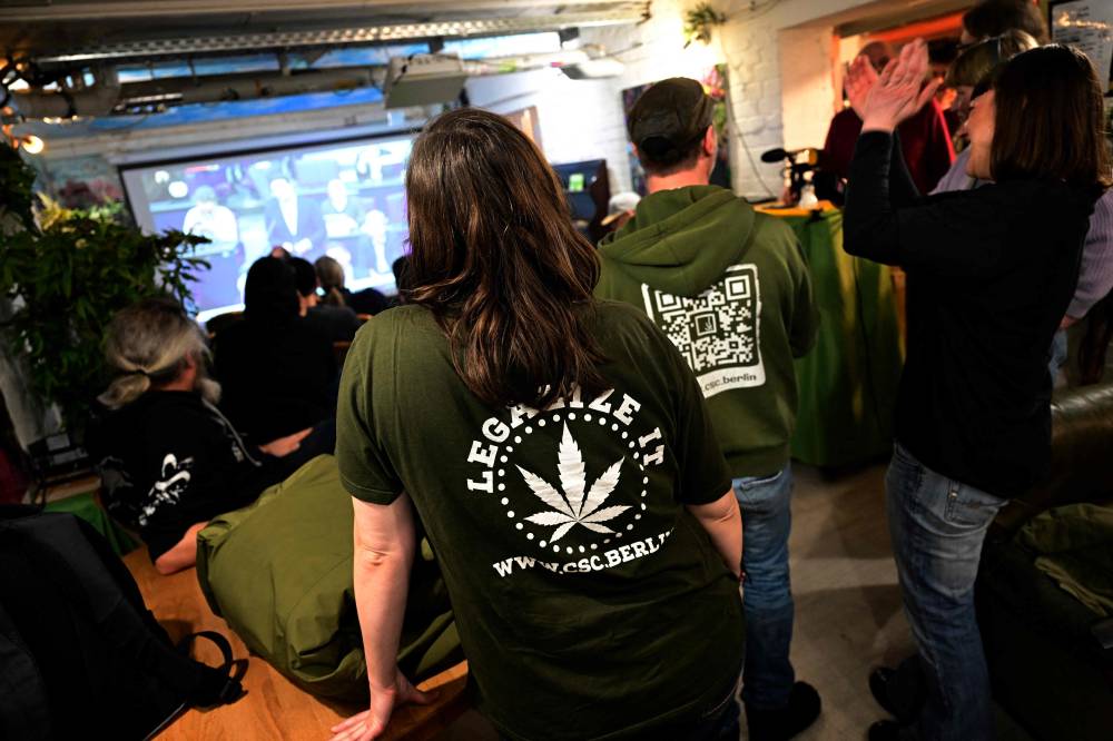 Staff members wearing clothes advertising for the legalization of Cannabis react as they watch a debate at the Bundestag (German lower house of parliament) on a screen, as the parliament scheduled the vote on decriminalisation of cannabis, on February 23, 2024 at the Berlin's Hemp Museum. (Photo by JOHN MACDOUGALL / AFP)