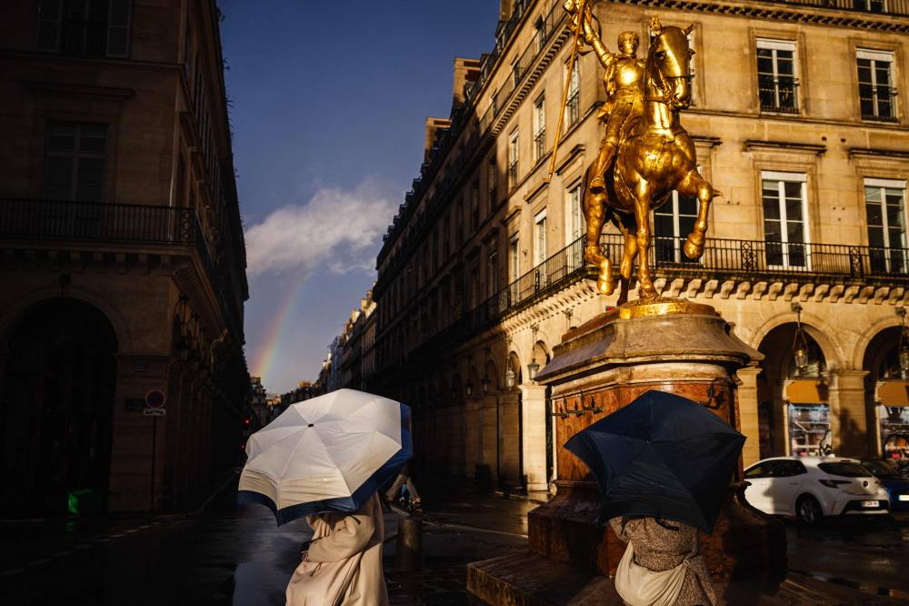 Pedestrians shelter from the rain and the wind under umbrellas, as they walk by the sculpture depicting Joan of Arc ("Le Monument a Jeanne d'Arc"), made by French sculptor Emmanuel Fremiet in 1874, in central Paris on Feb 22, 2024. (Photo by Dimitar DILKOFF / AFP)
