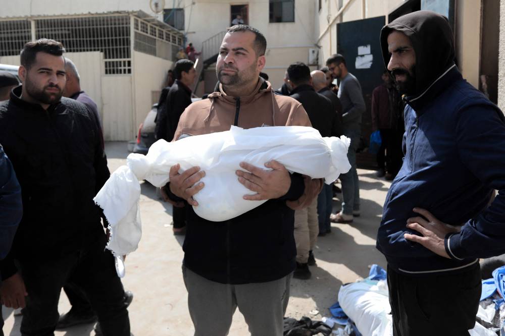 A man holds the shrouded body of a child killed during Israeli bombardment, outside Al-Aqsa hospital in Deir el-Balah in central Gaza. Photo by AFP