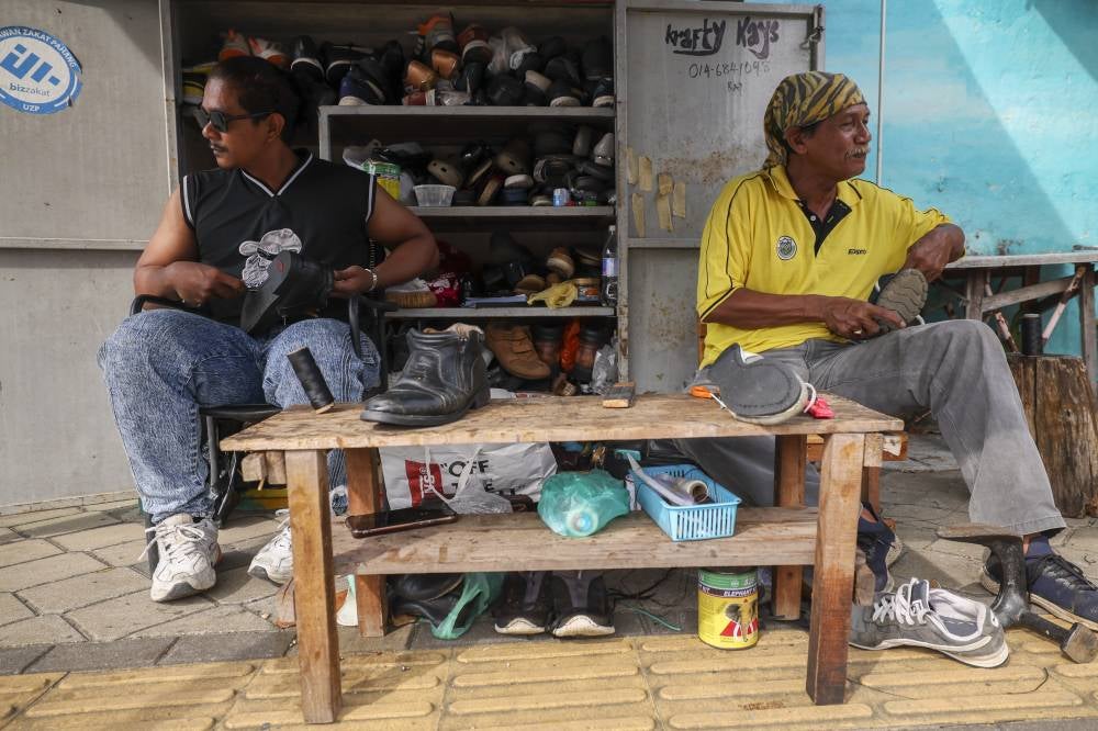 Adam (left) with his father Ali doing their the daily routine of cobbling shoes at the Kuantan Art Street here. Photo by Bernama