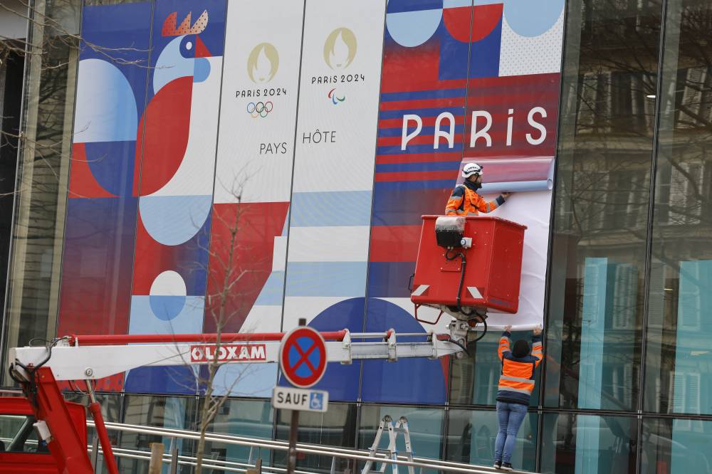 Workers set up a giant poster announcing the Olympic Games on the facade of the Solidarity and Health ministry in Paris, on Feb 27, 2024. - (Photo by LUDOVIC MARIN / AFP)