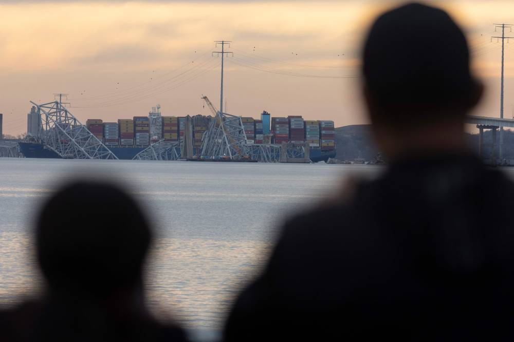People watch as the sun descends beyond the collapsed Francis Scott Key Bridge on March 28, 2024 in Baltimore, Maryland. - (Photo by SCOTT OLSON / AFP)