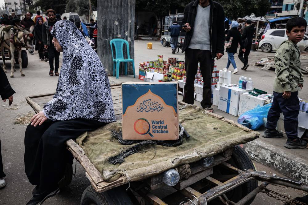 A Palestinian woman sits on a cart next to a box of food rations provided by US charity World Central Kitchen at a makeshift street market in Rafah in the southern Gaza Strip on March 14, 2024. - (Photo by MOHAMMED ABED / AFP)