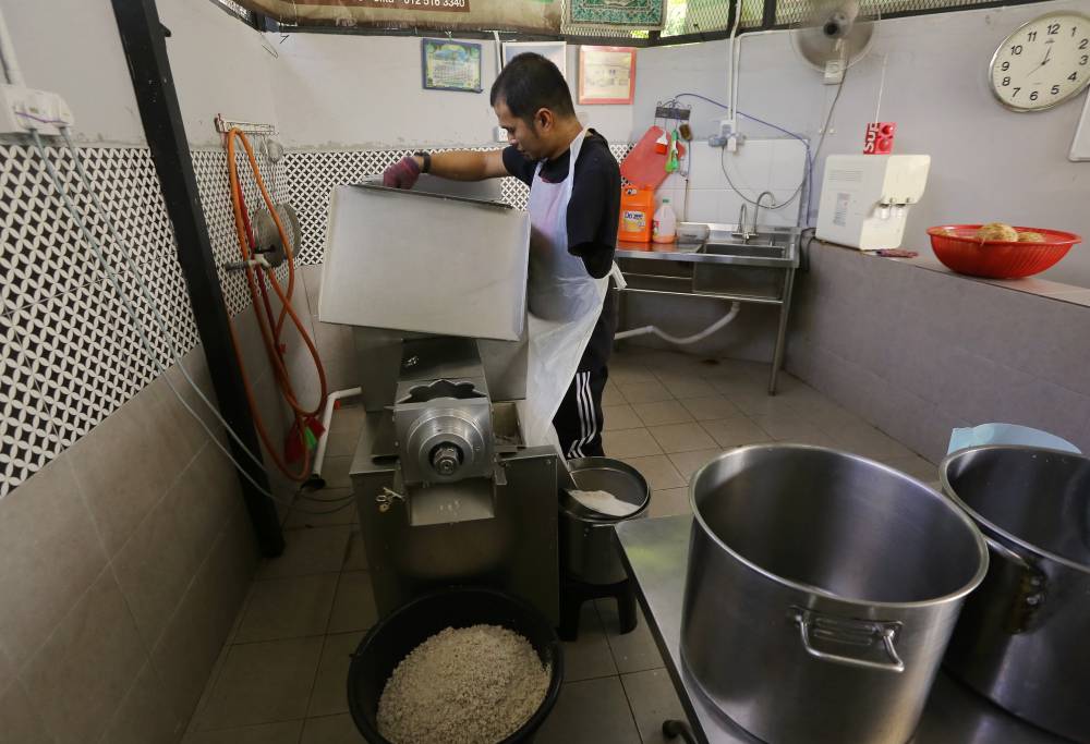 Owner of Santan M'darat Mohd Firdaus Ismail, 40, using the coconut milk extraction machine when met in Kampung Sungai Rokam, Ipoh. - Photo by Bernama