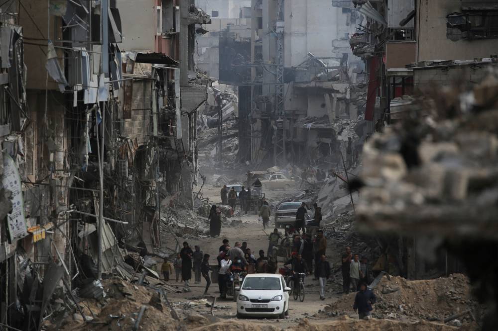 Palestinians walk past damaged buildings in Khan Yunis on April 8, 2024 after Israel pulled its ground forces out of the southern Gaza Strip. - Photo by AFP
