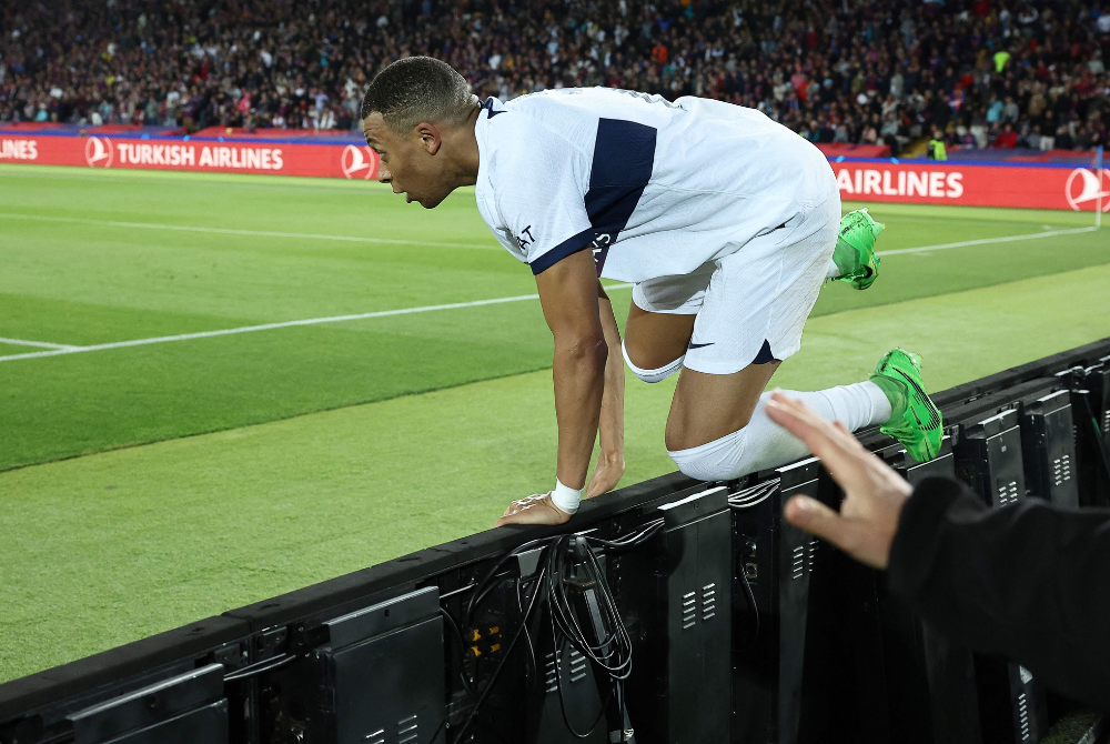 Paris Saint-Germain's French forward #07 Kylian Mbappe jumps the fence as he celebrates scoring his second goal and his team's fourth goal during the UEFA Champions League quarter-final second leg football match between FC Barcelona and Paris SG at the Estadi Olimpic Lluis Companys in Barcelona on April 16, 2024. (Photo by AFP)