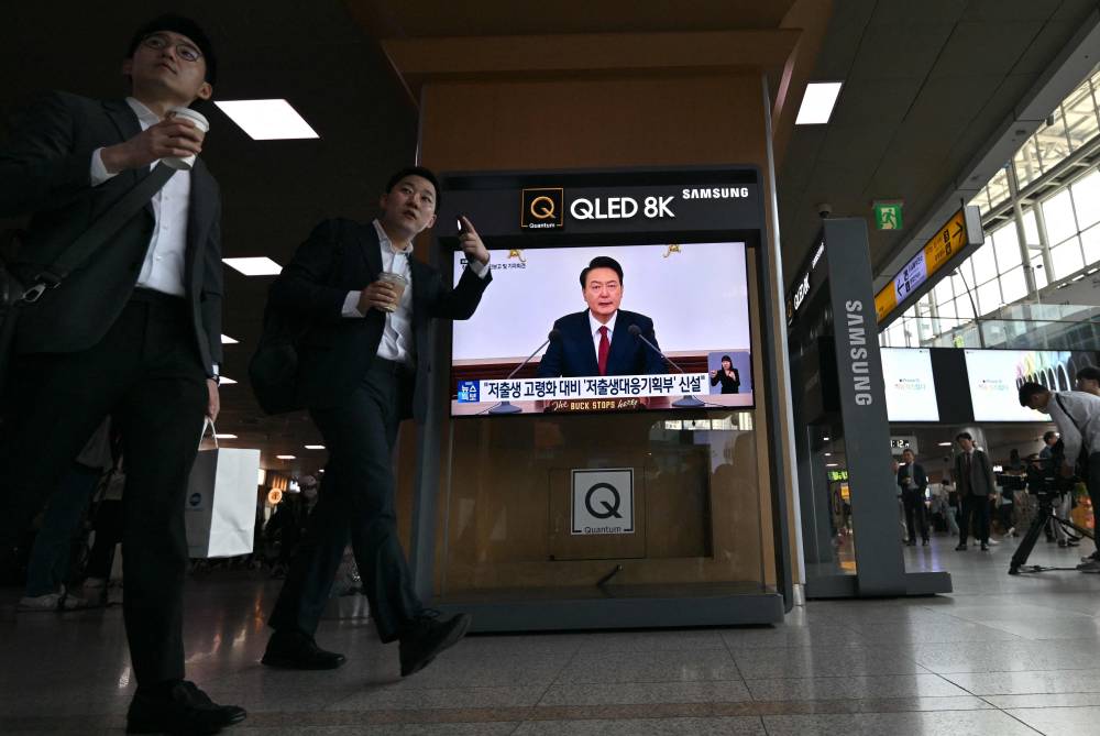 People walk past a television news screen broadcasting live footage of South Korean President Yoon Suk Yeol delivering a speech at a press briefing, at a railway station in Seoul on May 9, 2024. (Photo by Jung Yeon-je / AFP)